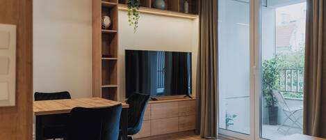 Una sala de estar moderna con una mesa de comedor, sillas, un televisor y un ventanal con cortinas.
