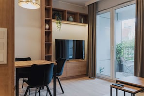A modern living room with a dining table, chairs, a television, and a large window with curtains. - RentPlanet - Apartament Dąbrowskiego (Poznań)