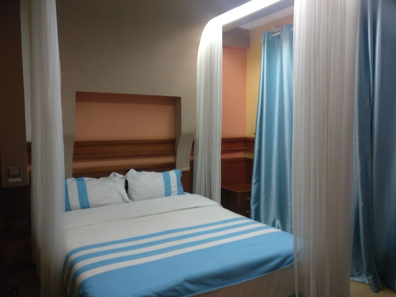A bed with a striped bedspread, a wooden headboard, and white curtains.