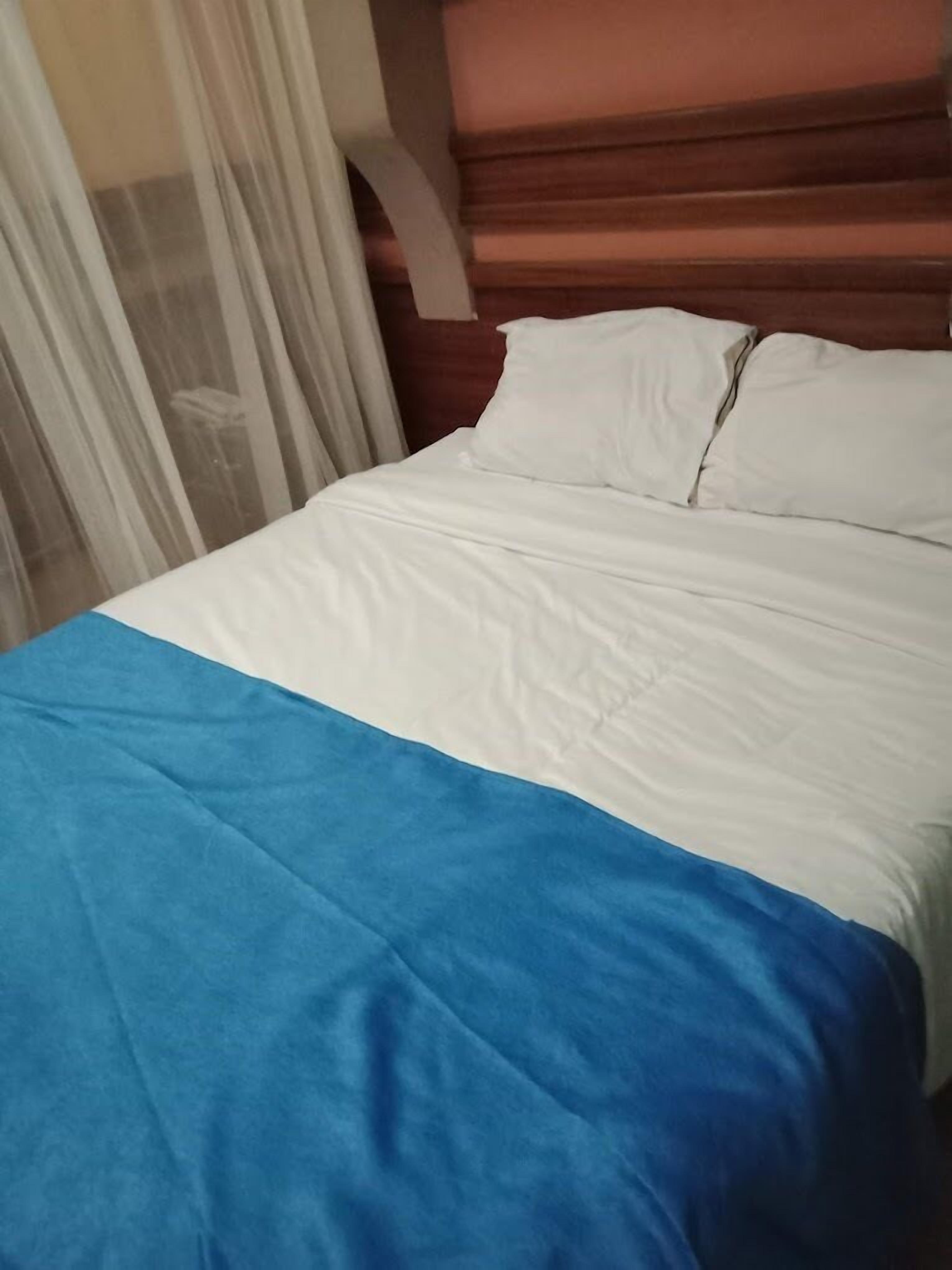 A bed with white and blue bedding, a wooden headboard, and sheer curtains.