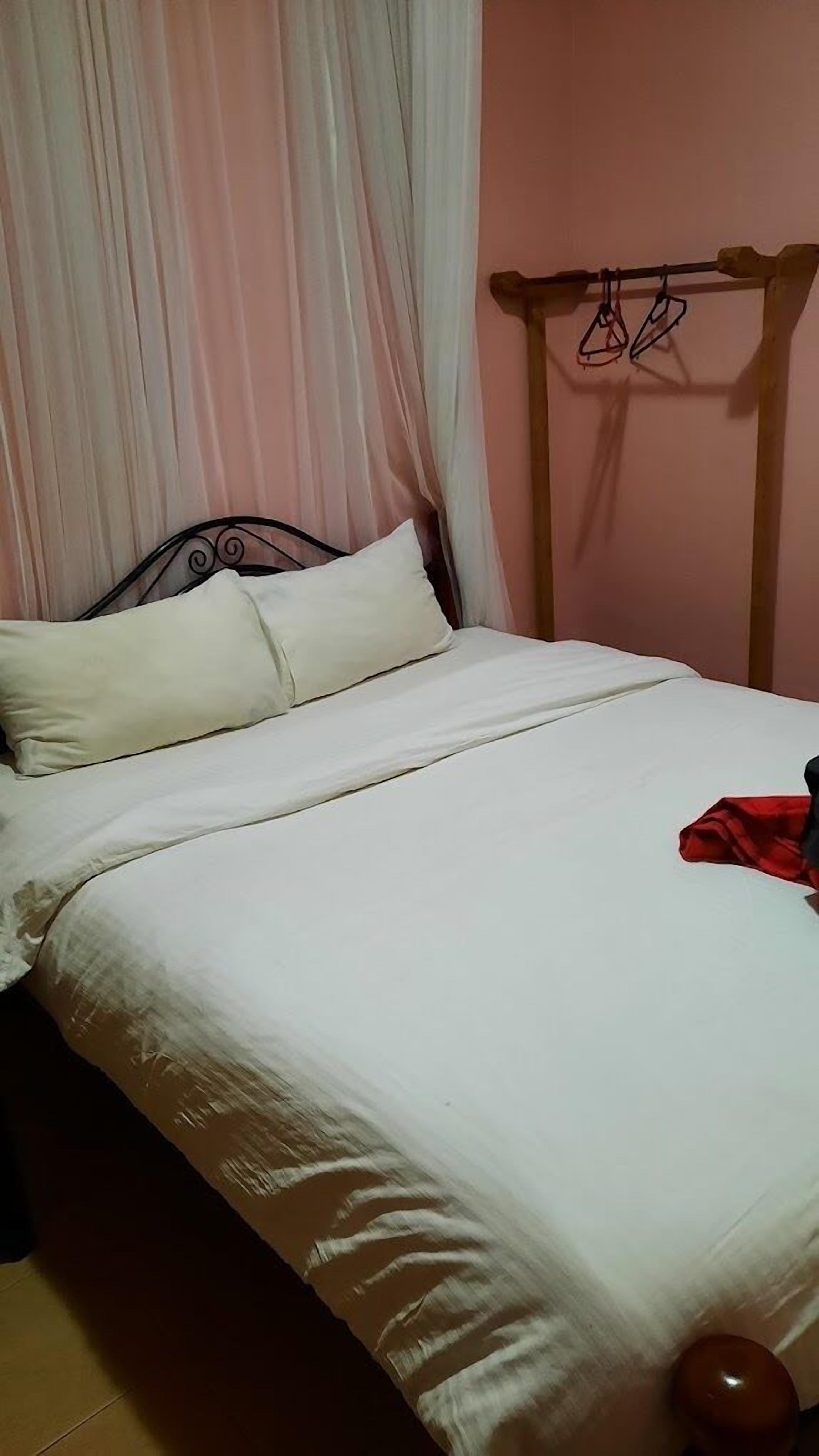 Una cama con ropa blanca, cabecera de madera y un objeto rojo a la derecha.