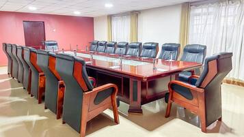 A conference room with a long table and multiple chairs, a red accent wall, and a large window with curtains.