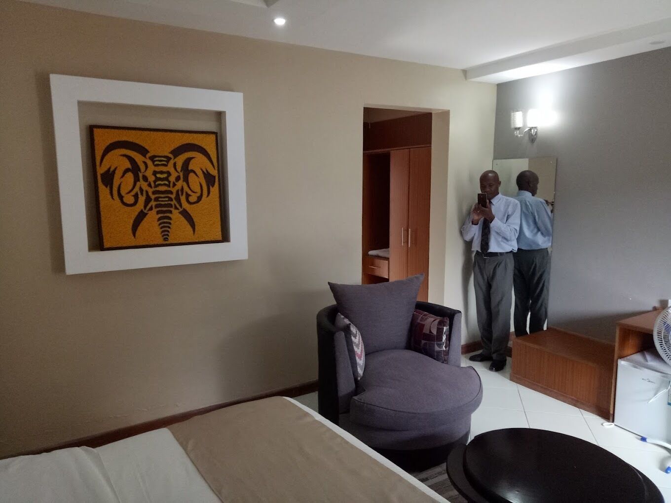 A hotel room with a bed, a chair, a wardrobe, and a mirror.