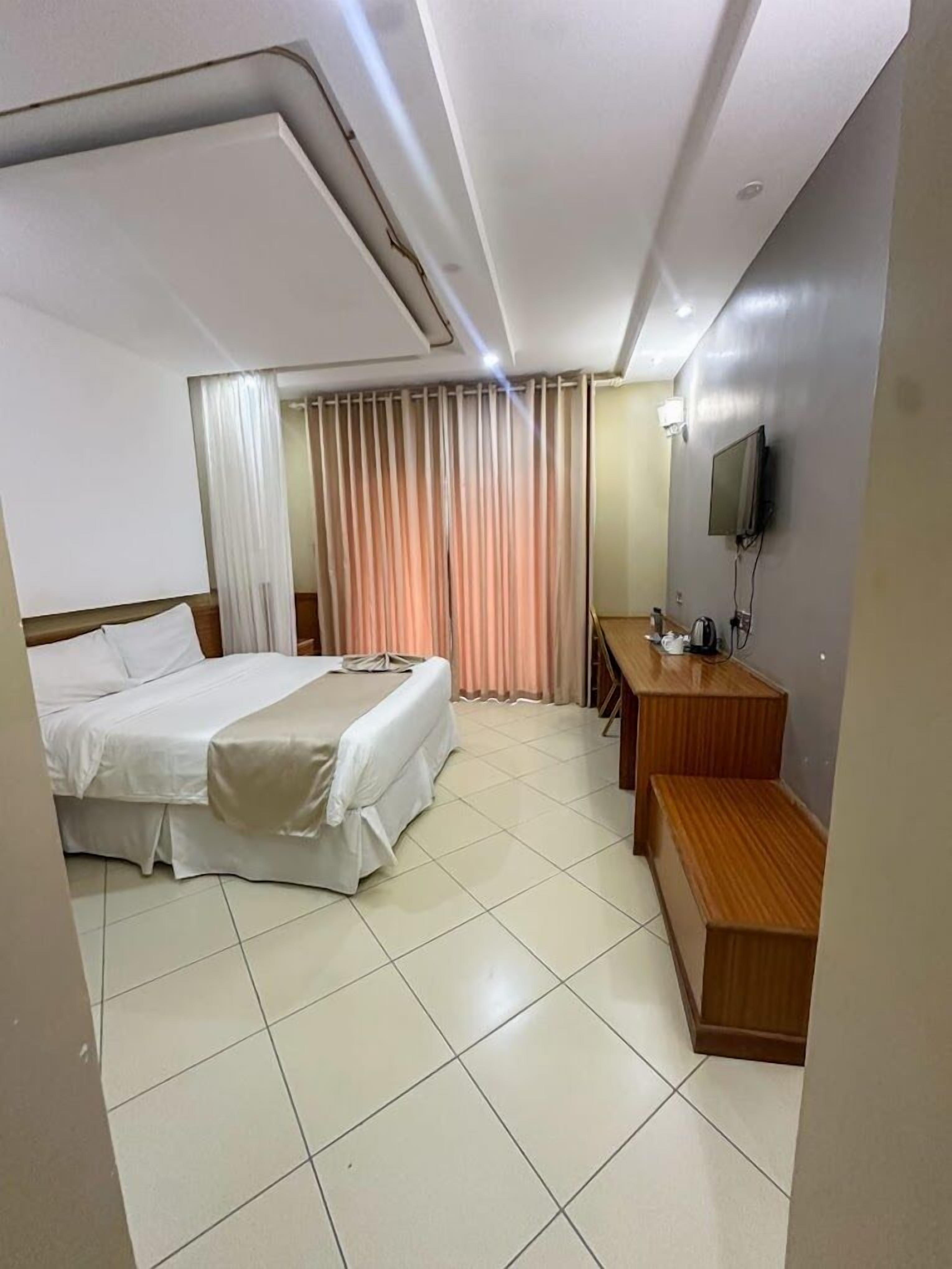 A hotel room with a bed, a desk, a chair, a television, and a window with curtains.