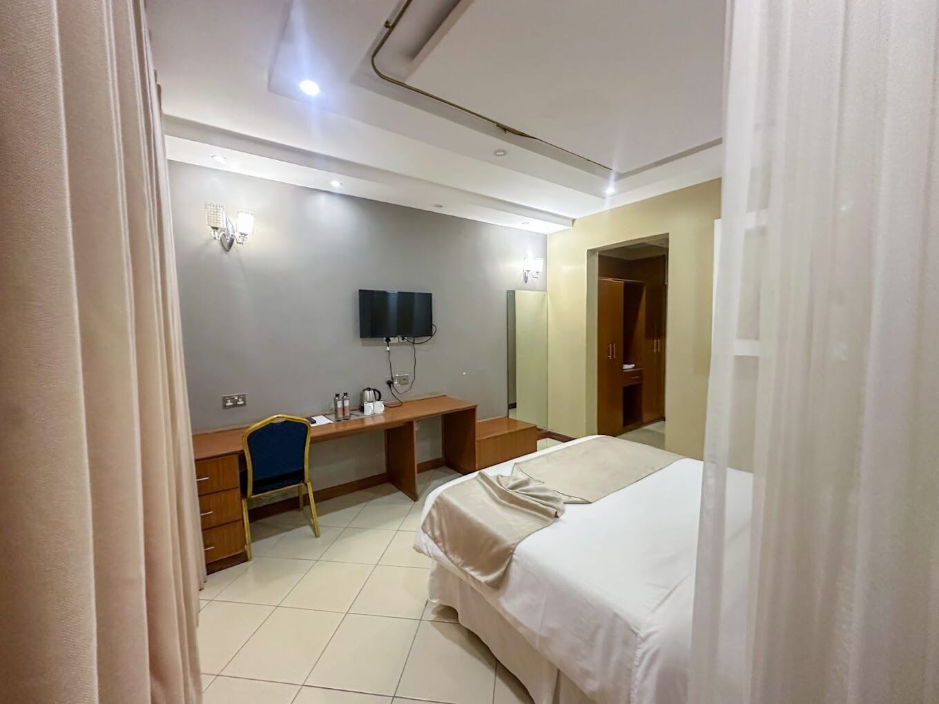 Une chambre d’hôtel comprenant un lit, un bureau avec une chaise, une télévision et une armoire.