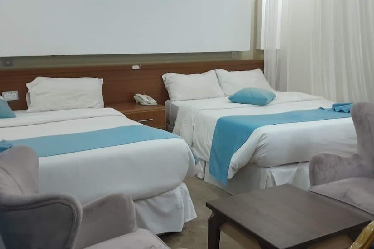 A hotel room with two beds, a small table, and a chair.