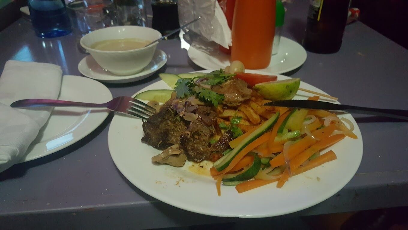 A plate of food with meat, vegetables, and a side dish on a table.