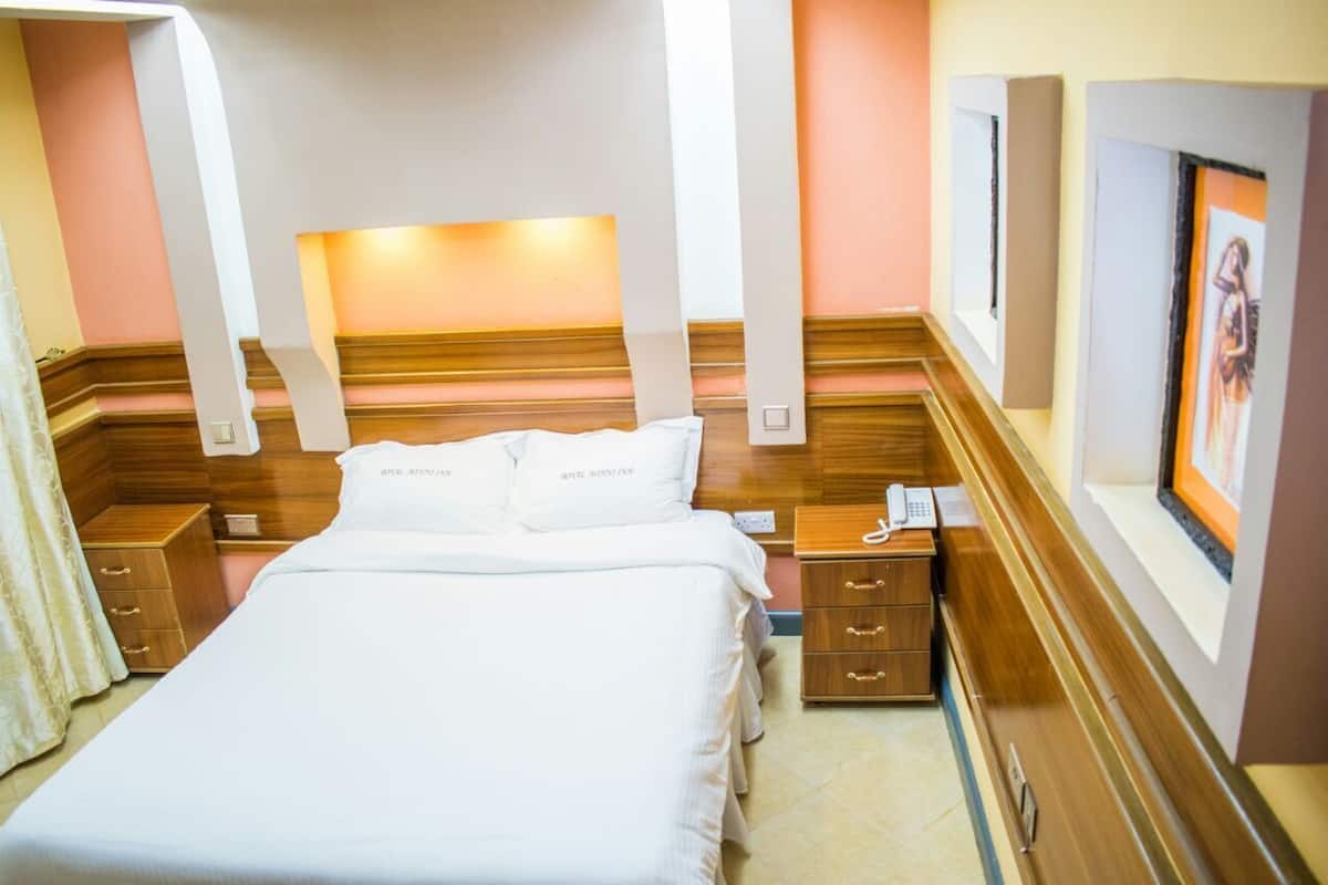 A hotel room with a large bed, wooden headboard, bedside tables, and a framed picture on the wall.