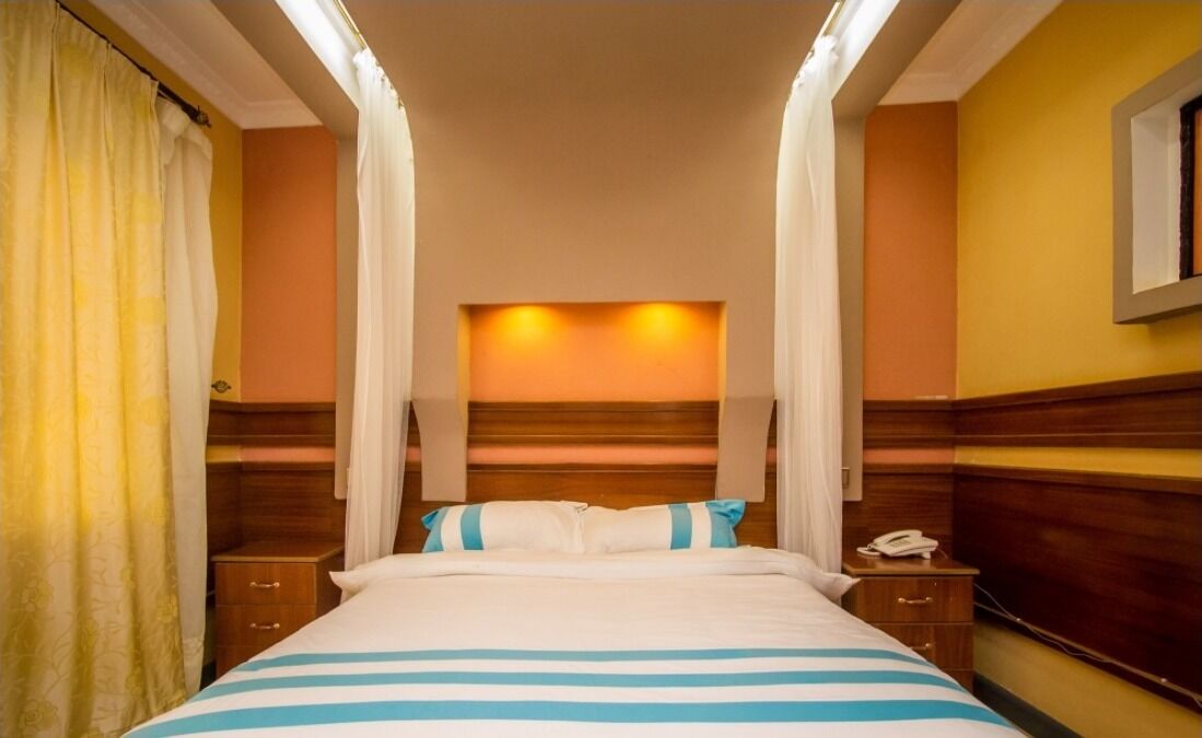 Habitación de hotel con cama, mesitas de noche, teléfono y cortinas.