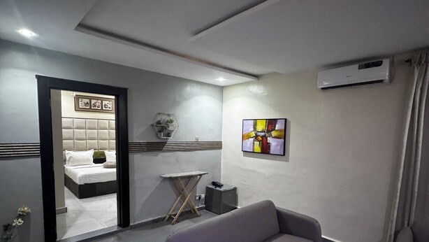 A modern hotel room with a sofa, a small table, an air conditioning unit, and a bed with a headboard.