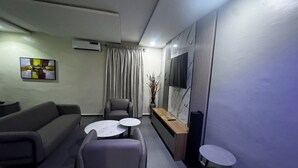 A modern living room with a sofa, two armchairs, a coffee table, and a TV on a wooden stand.