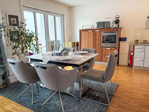 Una cocina moderna con comedor, que incluye una isla grande, sillas contemporáneas y vistas a través de un ventanal.