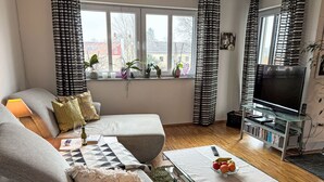 A modern living room with a sofa, a coffee table with fruit, a TV, and a bookshelf. - Ammerside by Interhome (Weilheim in Oberbayern)