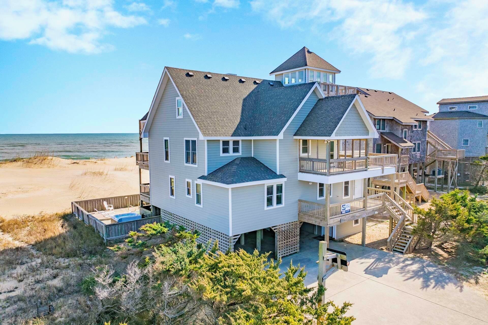 A multi-story beachfront house with a balcony, a small tower, and a pool area.