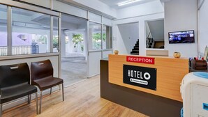 A hotel reception area with a reception desk, two chairs, a TV, and a staircase. - Super Hotel O Valasaravakkam Metro Mall (Chennai)