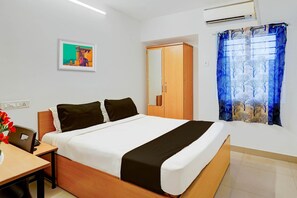 A hotel room with a bed, a wardrobe, a desk, a chair, a vase with flowers, and a painting on the wall. - Super Hotel O Valasaravakkam Metro Mall (Chennai)