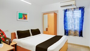 A hotel room with a bed, a desk, a chair, a wardrobe, a painting, and a window with a curtain. - Super Hotel O Valasaravakkam Metro Mall (Chennai)