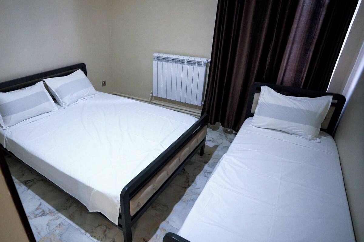 A room with two single beds, a radiator, and a curtain.