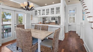 A modern kitchen with white cabinetry, a wooden dining table, wicker chairs, and a chandelier. - White Sails | 3BR Coastal Retreat in Destin Pointe (Destin)