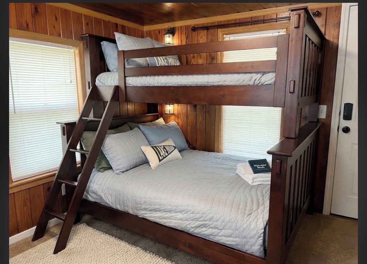 Una cama litera con escalera, una mesita de noche y una ventana con persianas.