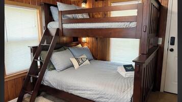 Una cama litera con escalera, una mesita de noche y una ventana con persianas.
