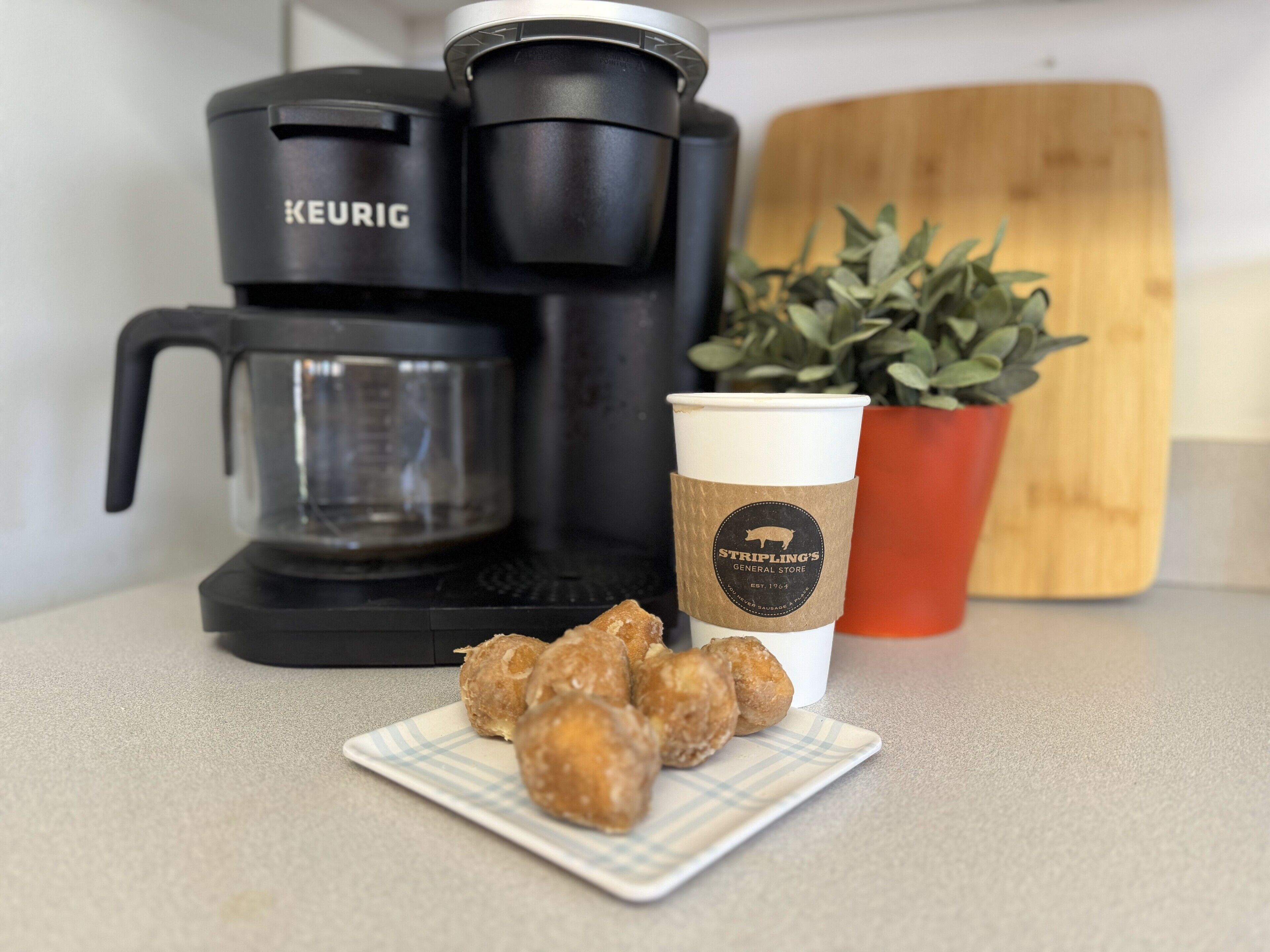 Uma cafeteira Keurig, uma chávena de café com logótipo e um prato de comida numa bancada.