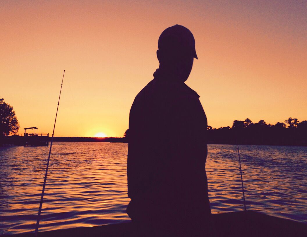 La silhouette d’une personne se tenant près d’une étendue d’eau au coucher du soleil.