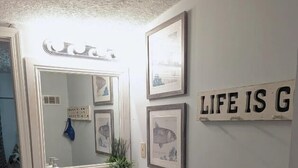 Ein Badezimmer mit weißem Waschtisch, einem großen Spiegel und gerahmten Fischzeichnungen an der Wand.