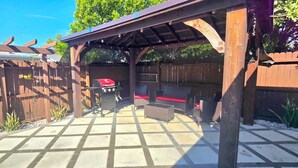 A covered patio area with a barbecue grill, outdoor furniture, and a wooden fence. - #39 The Farmington House (Port Richey)