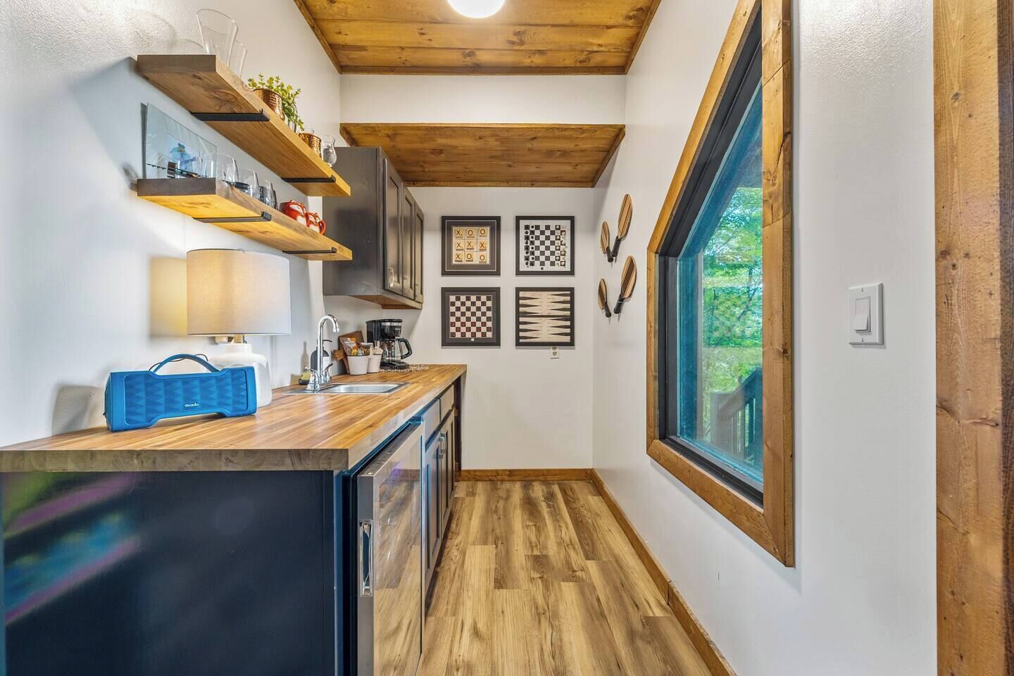 Una cocina estrecha con estantes de madera, un lavamanos y un ventanal.