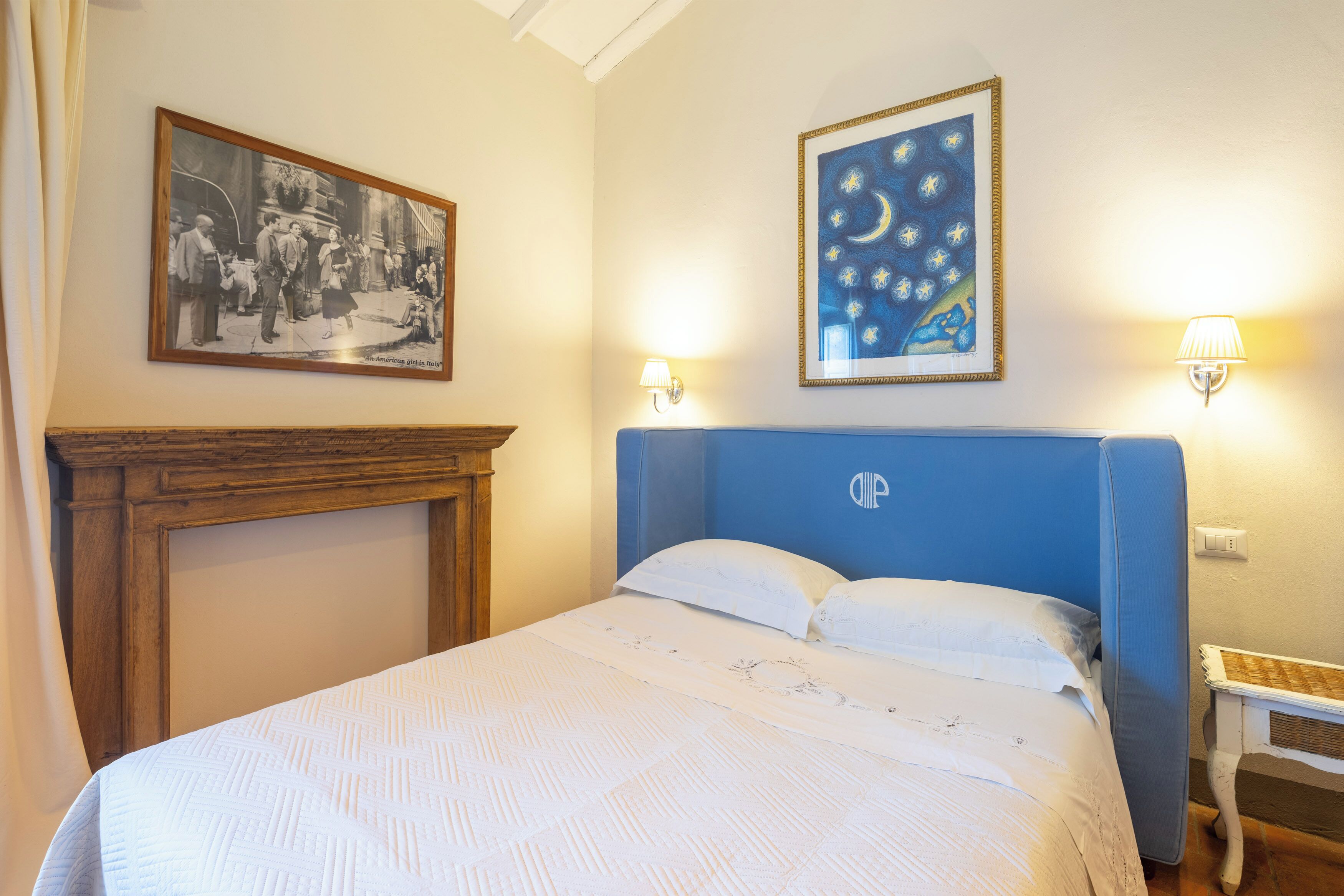 Ein Schlafzimmer mit Bett, Nachttisch, Lampe, einem gerahmten Bild und einem Kamin.