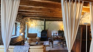 Ein rustikaler Raum mit Steinwänden, einem Kamin, einem Sofa, einem Esstisch und einer Lampe.