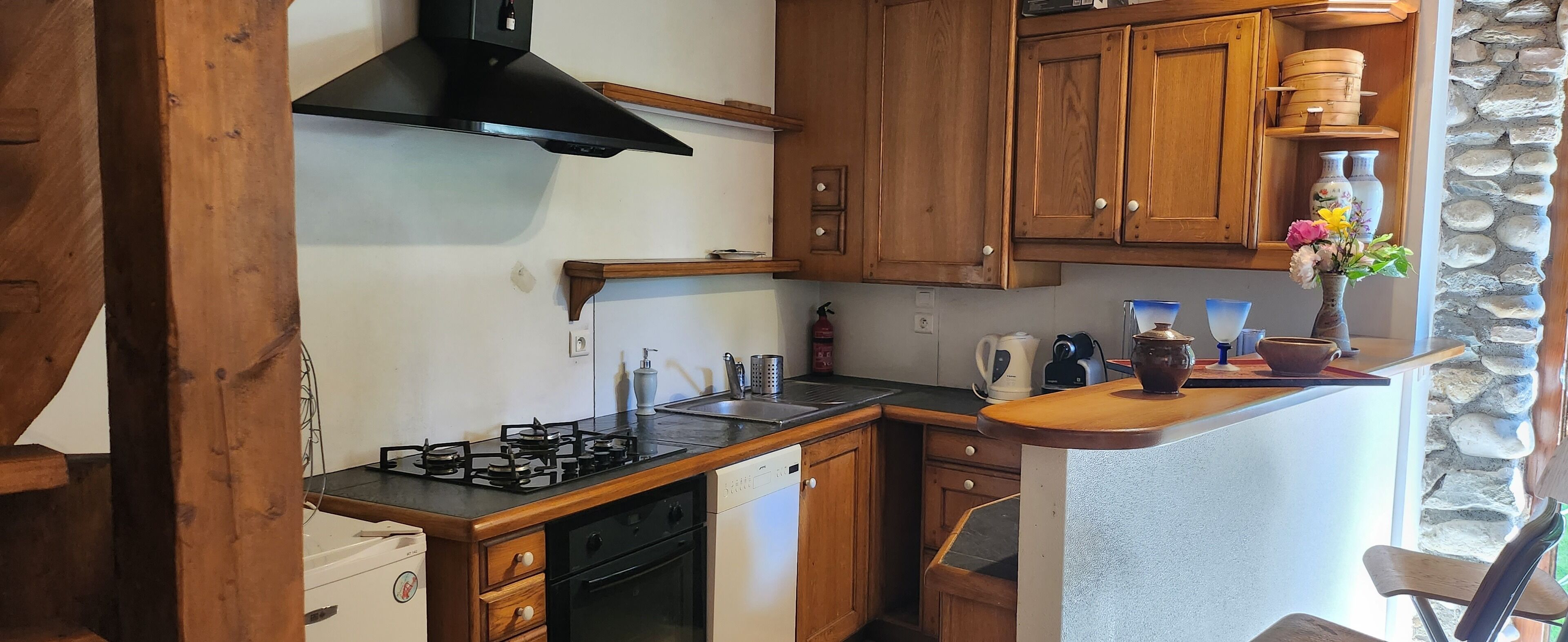 Une cuisine avec des meubles en bois, une cuisinière à gaz, un lave-vaisselle et un mur en pierre.