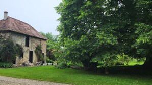 Ein Steinhaus mit Ziegeldach, umgeben von einem gepflegten Garten und einem großen Baum.
