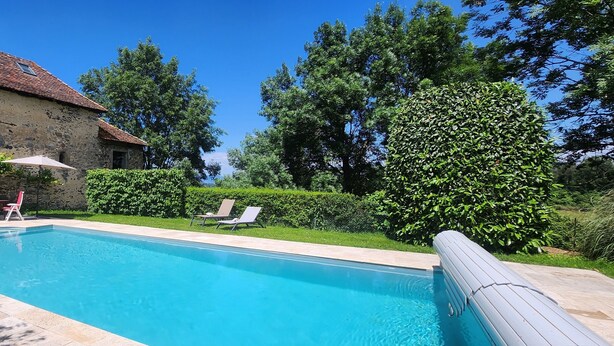 Ein Pool mit Liegestühlen, ein Steinhaus und üppige Bepflanzung.