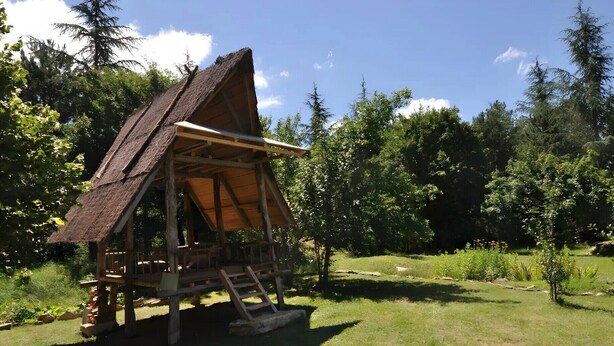 A rustic wooden structure with a thatched roof, surrounded by greenery and trees. - La Sylve Guest Room with Private Terrace, Shared Garden and Wi-Fi (Marcilhac sur Célé)