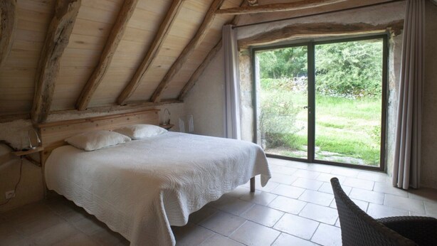 A bedroom with a bed, a chair, a window, and a view of greenery.