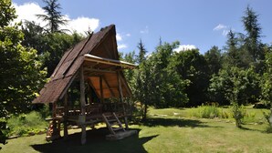 A wooden cabin with a thatched roof, surrounded by a grassy area and trees.