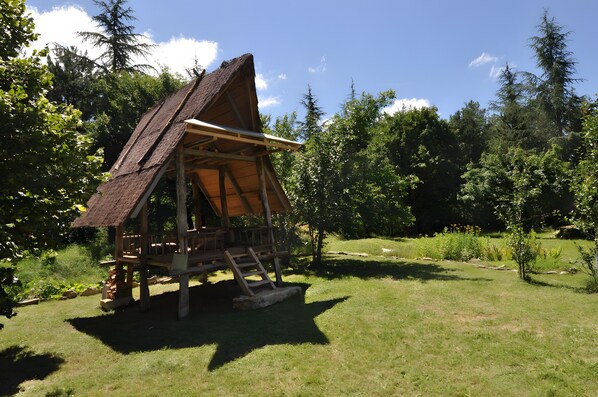 Een houten hut met rieten dak, omgeven door gras en bomen.