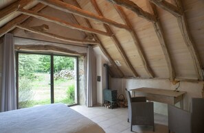 Een slaapkamer met een groot bed, een houten plafond, een raam en uitzicht op groen.