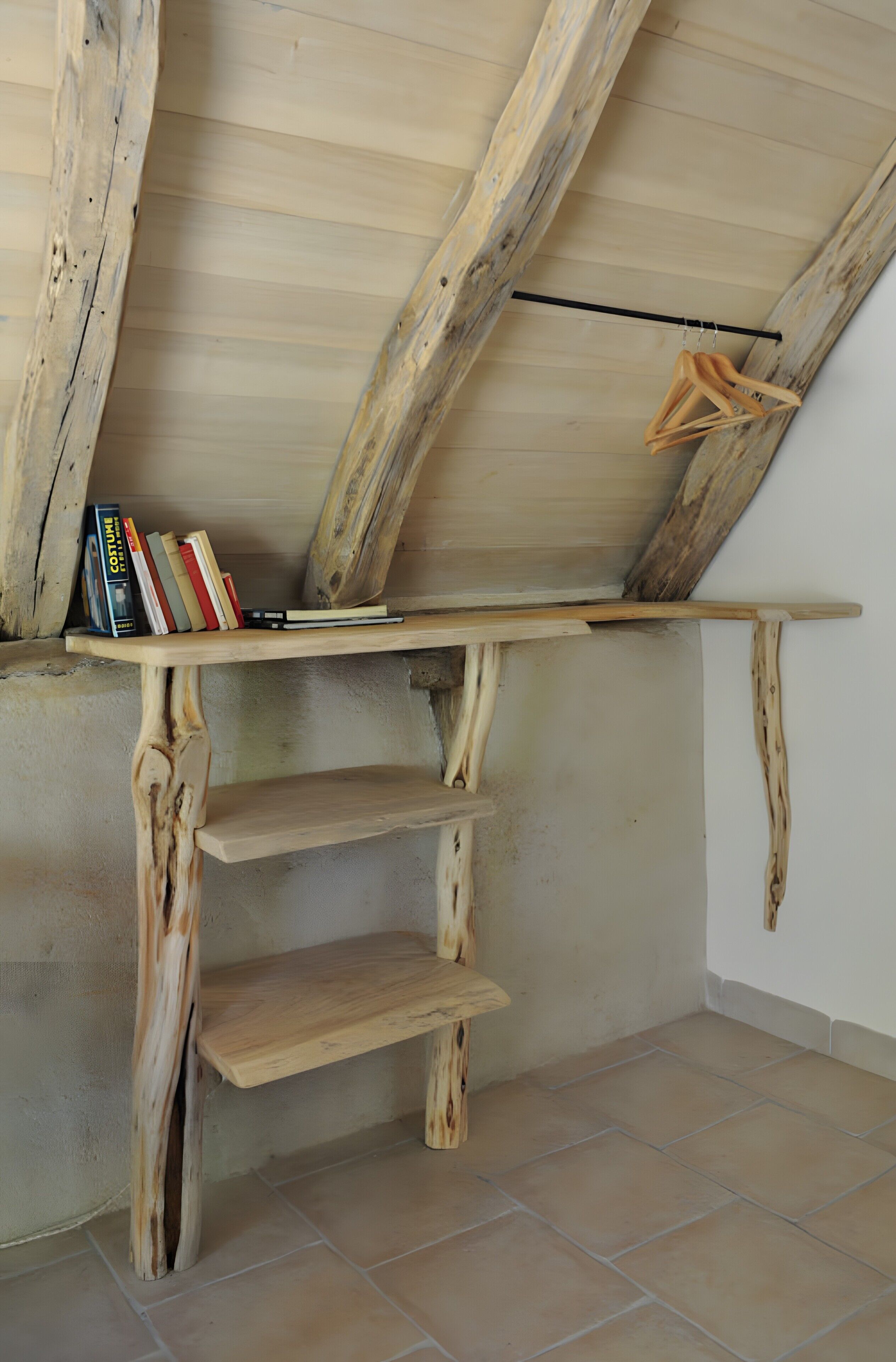 Een rustiek houten plank met boeken en kledinghangers, een schuin plafond en een betegelde vloer.