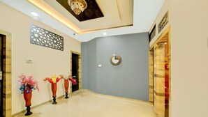 A hotel lobby with a modern design, featuring a light blue wall, decorative vases with flowers, and a ceiling with recessed lighting. - Collection O Vrindavan Palace Colony (Indore)