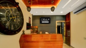 A reception area with a large wall clock, a wooden reception desk, and a sign that reads "Collection Company-Serviced". - Collection O Vrindavan Palace Colony (Indore)