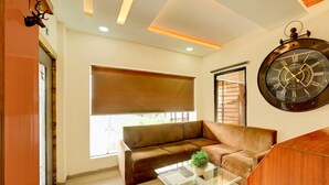A modern living room with a brown leather sofa, a glass coffee table with a plant, and a large wall clock. - Collection O Vrindavan Palace Colony (Indore)