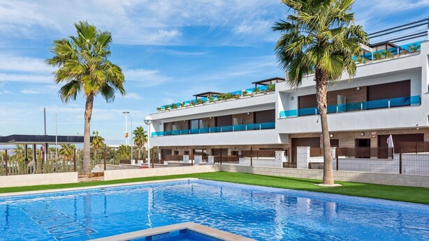 Et moderne hotel med swimmingpool, palmer og en klar blå himmel.