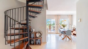 Un intérieur moderne avec un escalier en colimaçon, un coin repas comprenant une table et des chaises, et une vue dégagée grâce à de grandes fenêtres.