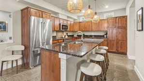 A modern kitchen with wooden cabinets, stainless steel appliances, a granite countertop, and bar stools. - Ember & Ash Designer Home w/ King Beds, Games (Fort Collins)