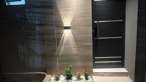 Une entrée moderne avec une porte en verre, un luminaire et un petit espace aménagé en jardin.