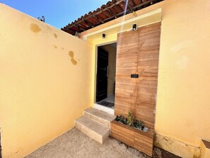 A yellow exterior wall with a wooden door and steps leading to a covered entrance. - AirBNBusiness Maracanaú (Maracanau)