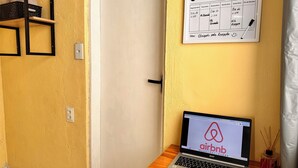A laptop on a wooden shelf displaying the Airbnb logo, a wall calendar with a weekly schedule, and a door with a handle.